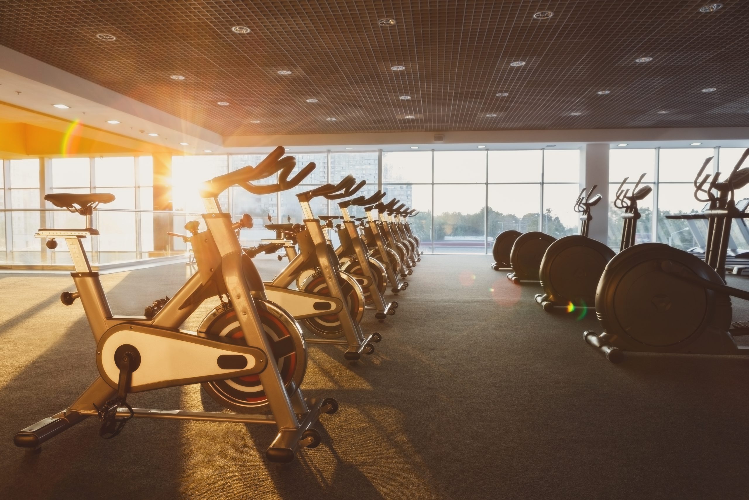 Modern gym interior with equipment. Fitness club with training exercise bikes, backlight in evening sunlight.